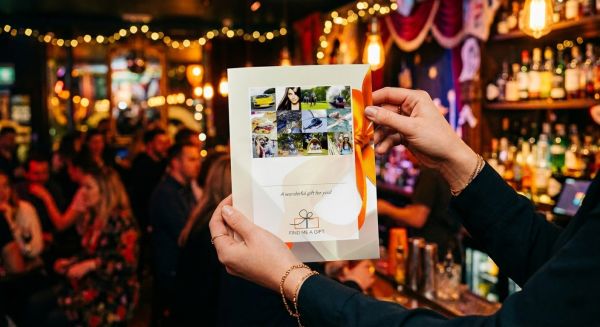 Hands holding a gift voucher in front of a blurred cocktail bar