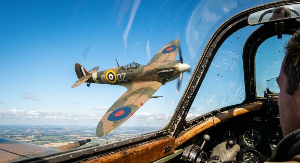 A vintage Spitfire flying closely alongside another aircraft in a clear blue sky