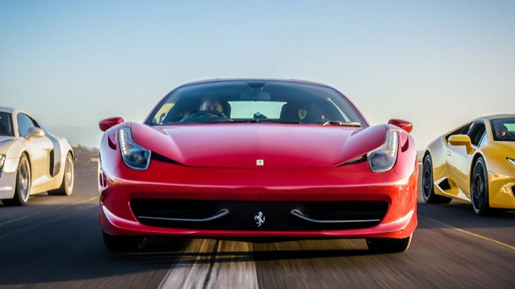 Luxury sports cars on highway – red Ferrari 458, yellow Lamborghini Huracán, and white Audi R8 driving fast at sunset