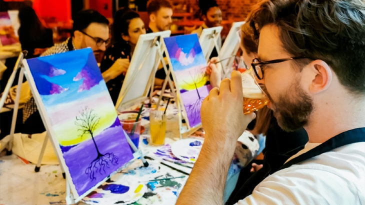 Man drinking beer with a group enjoying a fun sip and paint experience, creative group activity and unique gift idea